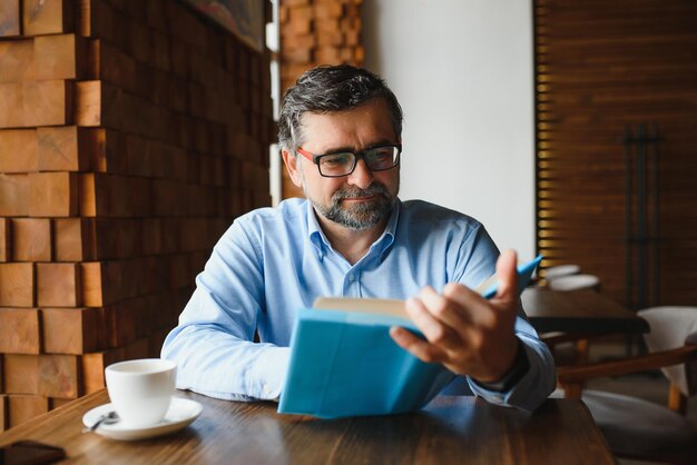 Uomo bello maturo che legge un libro in un caffè