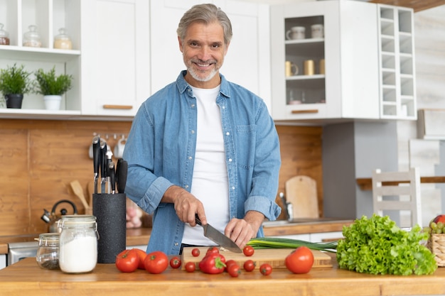 Uomo bello maturo dai capelli grigi che prepara cibo delizioso e sano nella cucina di casa.