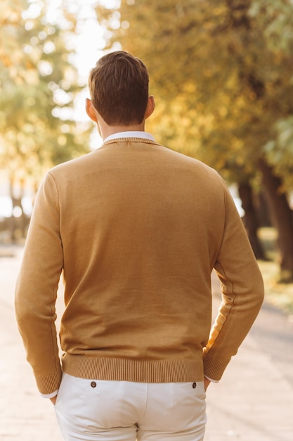 Uomo bello moderno in abiti gialli e bianchi in posa nel parco al tramonto