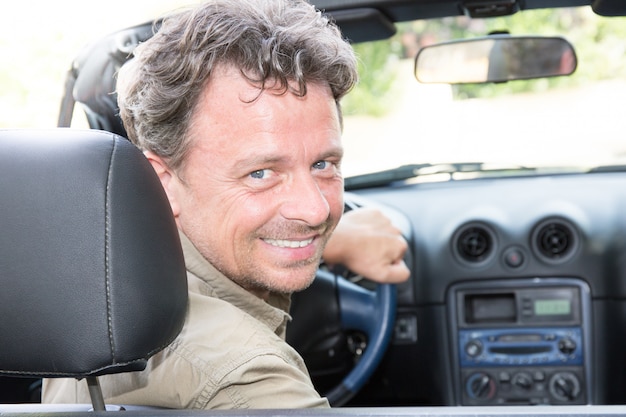 Uomo bello nel sorridere dell'automobile convertibile