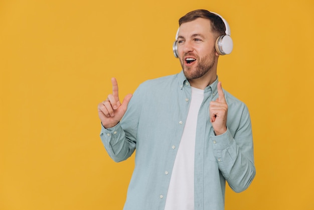 Uomo bello non rasato in camicia a menta che ascolta musica con le cuffie e indica con le dita lo spazio di copia su sfondo giallo