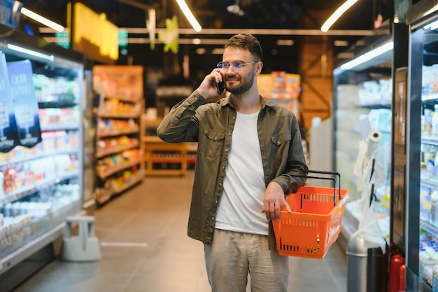 Uomo bello shopping nel supermercato smilling utilizzando il telefono