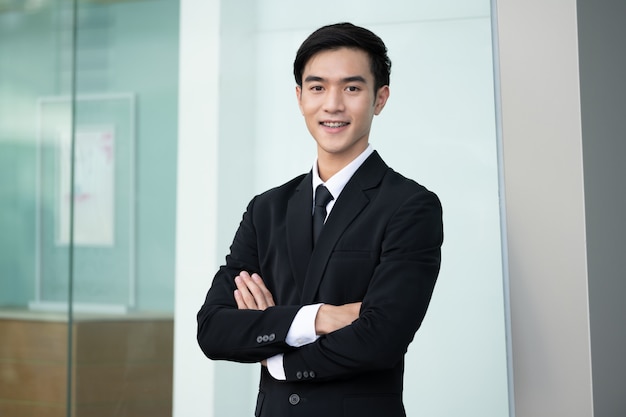 Uomo bello sicuro di affari che smilling in vestito nero che sta nell'ufficio