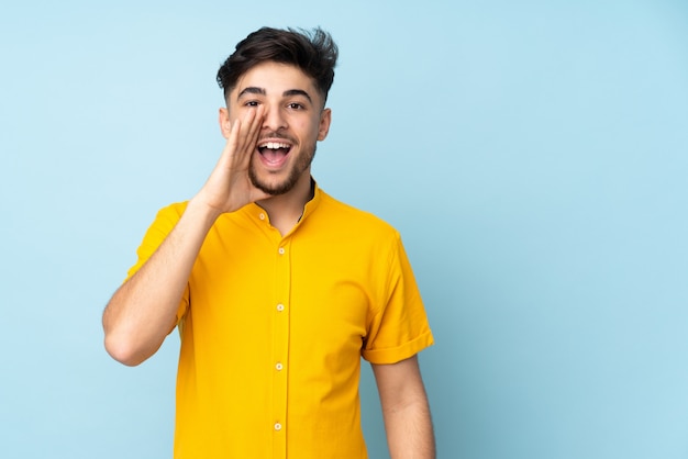 Uomo bello sopra la parete isolata che grida con la bocca spalancata