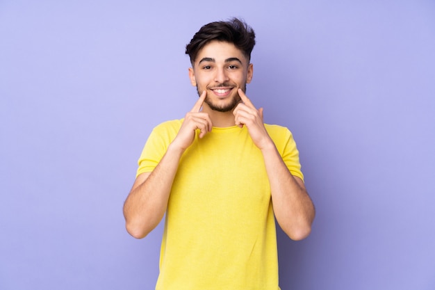 Uomo bello sopra la parete isolata che sorride con un'espressione felice e piacevole