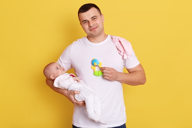 Uomo bello sorridente che indossa abbigliamento casual si leva in piedi contro il muro giallo