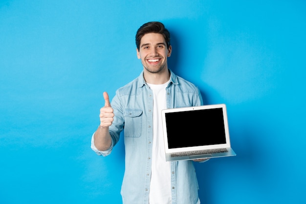 Uomo bello sorridente che mostra lo schermo e il pollice del laptop