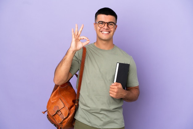 Uomo bello studente su sfondo isolato che mostra segno ok con le dita