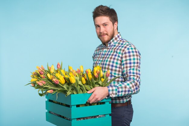 Uomo bianco bello che tiene una scatola con i tulipani gialli sulla superficie blu