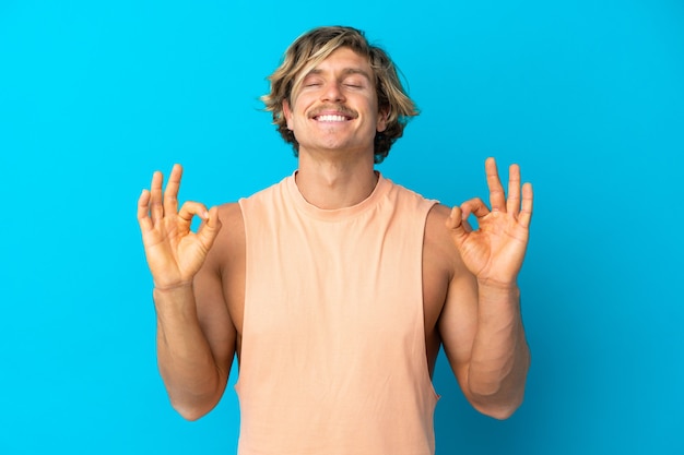 Uomo biondo bello isolato sull'azzurro nella posa di zen