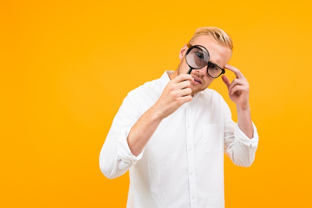 Uomo biondo che indossa una classica camicia bianca con gli occhiali guardando attraverso una lente di ingrandimento onyellow