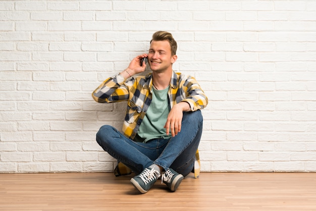 Uomo biondo che si siede sul pavimento mantenendo una conversazione con il telefono cellulare