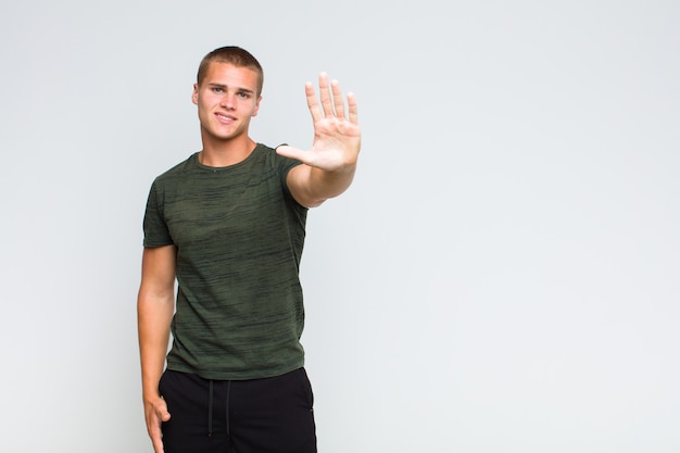 Uomo biondo che sorride e sembra amichevole, mostrando il numero cinque o quinto con la mano in avanti, contando alla rovescia