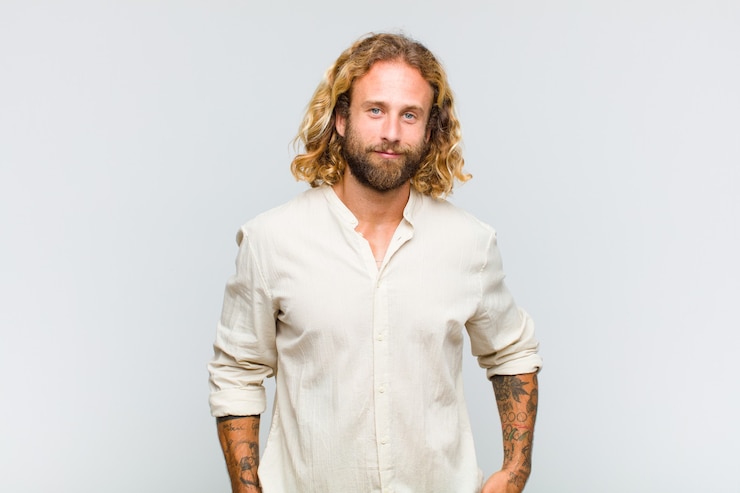 Foto uomo biondo che sorride positivamente e con sicurezza, guardando soddisfatto, amichevole e felice