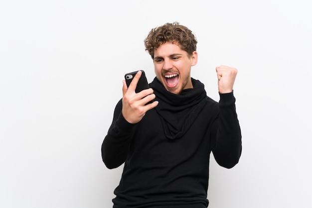 Uomo biondo con il telefono in posizione di vittoria