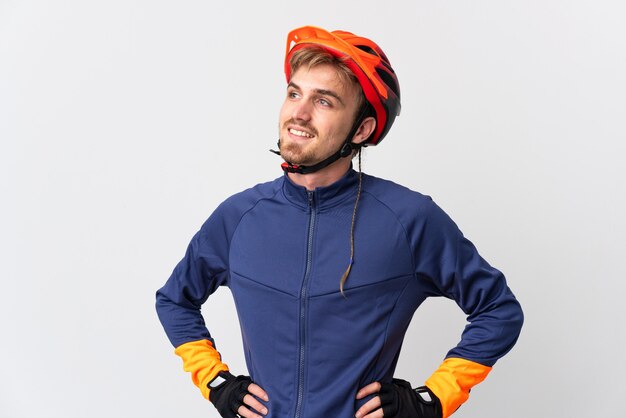 Uomo biondo giovane ciclista isolato su bianco in posa con le braccia al fianco e sorridente