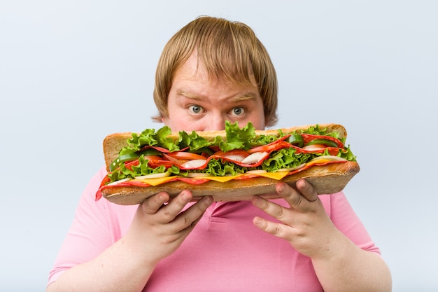 Uomo biondo pazzo caucasico che tiene un panino gigante