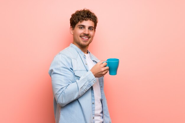 Uomo biondo sopra la parete rosa che tiene una tazza di caffè calda