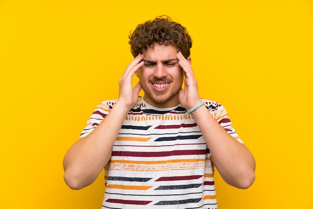 Uomo biondo sopra muro giallo infelice e frustrato con qualcosa. Espressione facciale negativa
