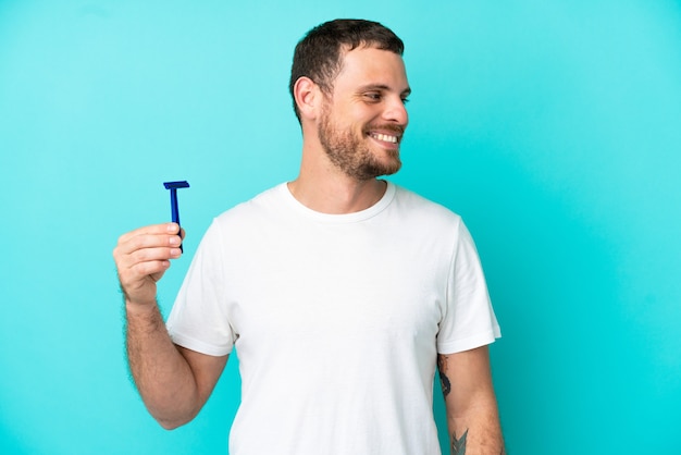 Uomo brasiliano che si rade la barba isolato su sfondo blu che guarda di lato