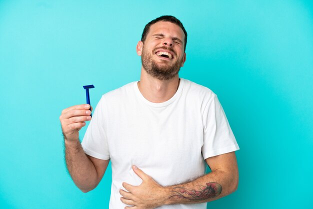 Uomo brasiliano che si rade la barba isolato su sfondo blu sorridendo molto