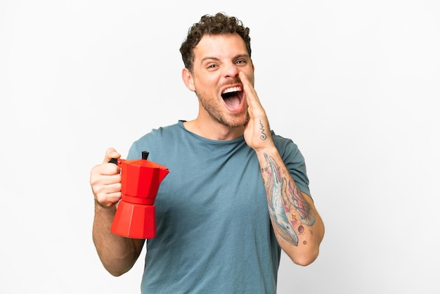 Uomo brasiliano che tiene caffettiera su sfondo bianco isolato gridando con la bocca spalancata