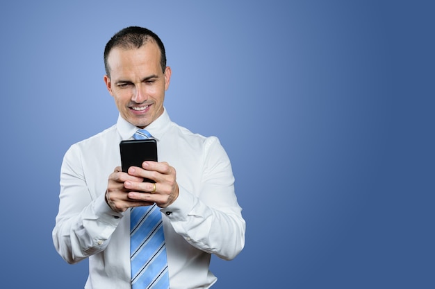 Uomo brasiliano maturo che indossa abiti formali, cravatta e guardando il suo smartphone. Sfondo blu.