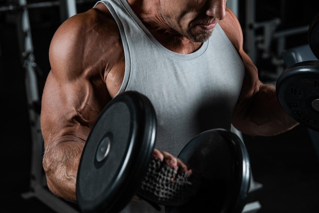 Uomo brutale adulto muscoloso con manubri pompe bicipiti in palestra Ritratto di autentico bodybuilder caucasico che fa esercizi di allenamento