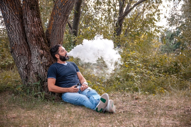 Uomo brutale alla moda che fuma una sigaretta elettronica. All'uomo piace molto il processo del fumo.