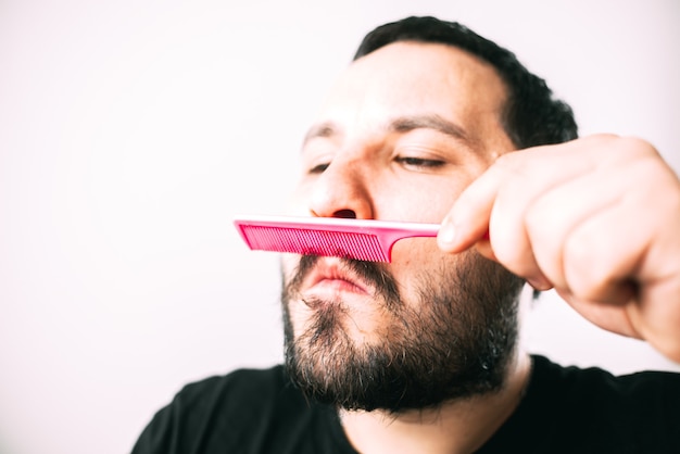 uomo brutale con gli occhiali che si pettina la barba con un pettine rosa