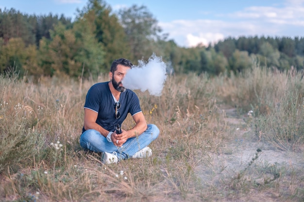 Uomo brutale di vape che fuma una sigaretta elettronica all'aperto.