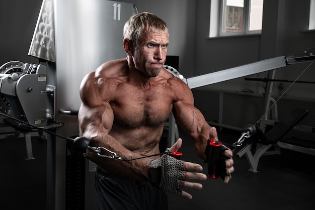 Uomo brutale muscolare adulto che si allena sui loop TRX in palestra Ritratto di autentico bodybuilder caucasico che fa esercizi in allenamento HIIT