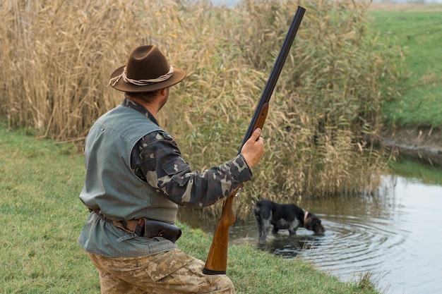 Uomo cacciatore in mimetica con una pistola durante la caccia alla ricerca di uccelli selvatici o selvaggina Stagione di caccia autunnale