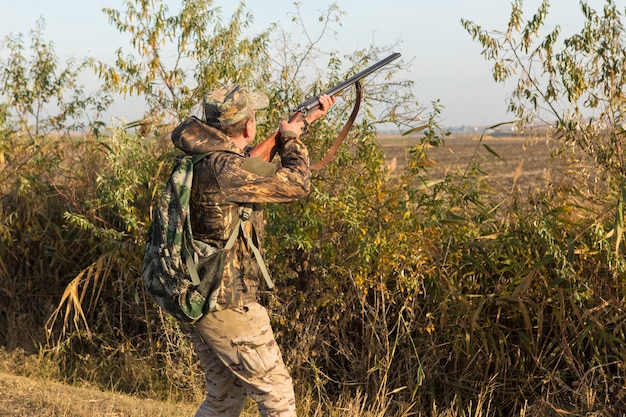 Uomo cacciatore in mimetica con una pistola durante la caccia alla ricerca di uccelli selvatici