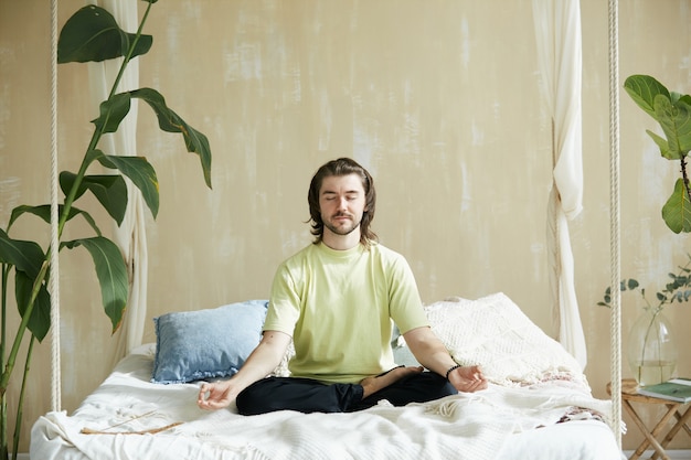 Uomo calmo e rilassato seduto a letto e meditando, concetto di salute mentale e armonia che vive con la meditazione tecaher