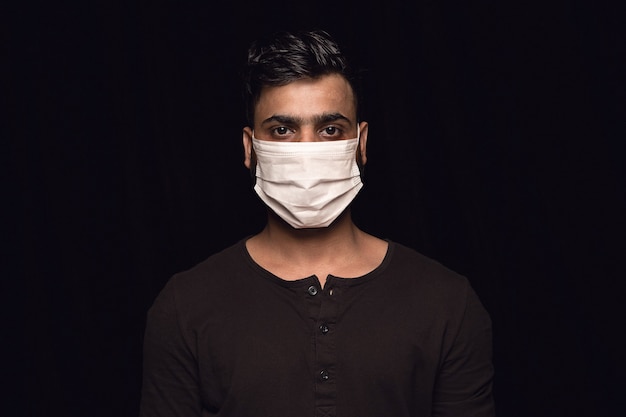 Uomo calmo in maschera protettiva su sfondo nero. Prevenzione contro la polmonite, continuate a stare in quarantena, restando a casa. Trattamento cinese del coronavirus. Sanità, medicina, concetto di isolamento.