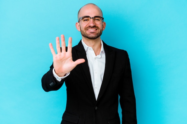 Uomo calvo caucasico di giovani affari isolato sulla parete blu sorridente allegro che mostra numero cinque con le dita.