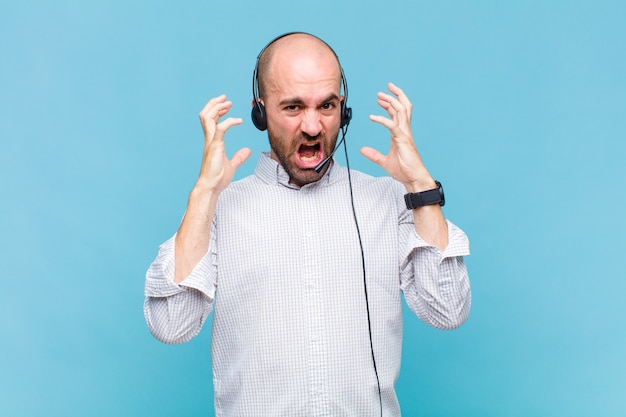 Uomo calvo che grida con le mani in aria, sentendosi furioso, frustrato, stressato e sconvolto