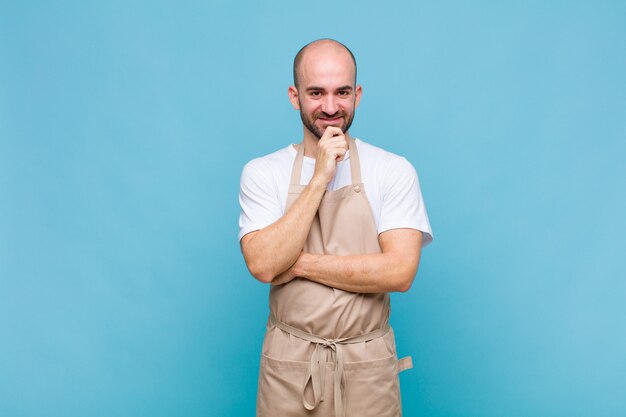 Uomo calvo che sembra felice e sorridente con la mano sul mento, chiedendosi o facendo una domanda, confrontando le opzioni