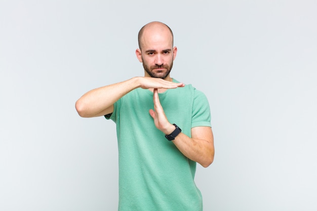 Uomo calvo che sembra serio, severo, arrabbiato e dispiaciuto, facendo segno di time out