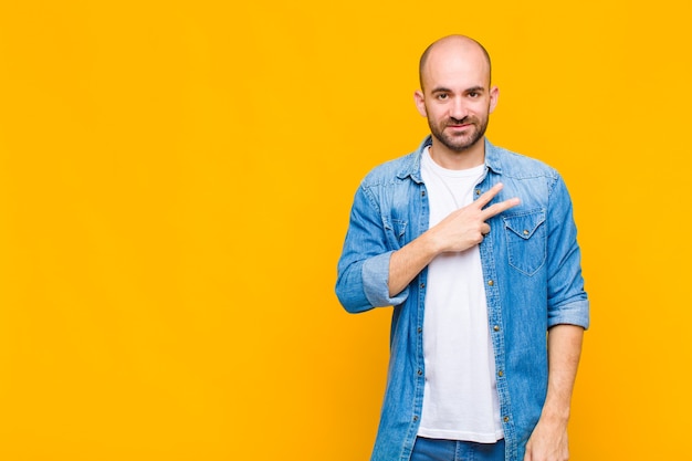 Uomo calvo che si sente felice, positivo e di successo, con la mano a forma di v sul petto, mostrando vittoria o pace