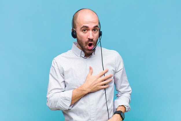 Uomo calvo che si sente scioccato e sorpreso, sorride, prende la mano sul cuore, felice di essere l'unico o di mostrare gratitudine