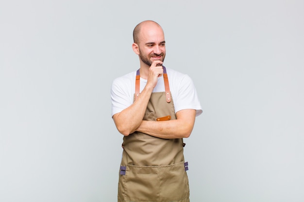 Uomo calvo che sorride con un'espressione felice e sicura con la mano sul mento, chiedendosi e guardando di lato