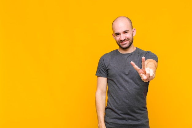 Uomo calvo che sorride e che sembra felice, spensierato e positivo, gesticolando vittoria o pace con una mano