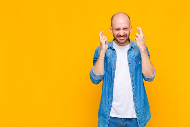 Uomo calvo che sorride e incrocio ansiosamente entrambe le dita, sentendosi preoccupato e desiderando o sperando buona fortuna