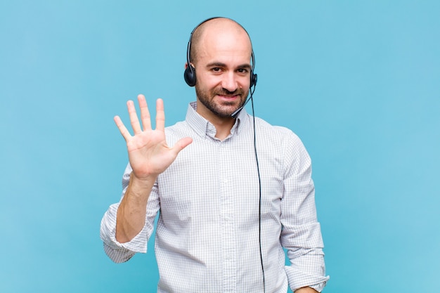 Uomo calvo che sorride e sembra amichevole, mostrando il numero cinque o quinto con la mano in avanti, conto alla rovescia