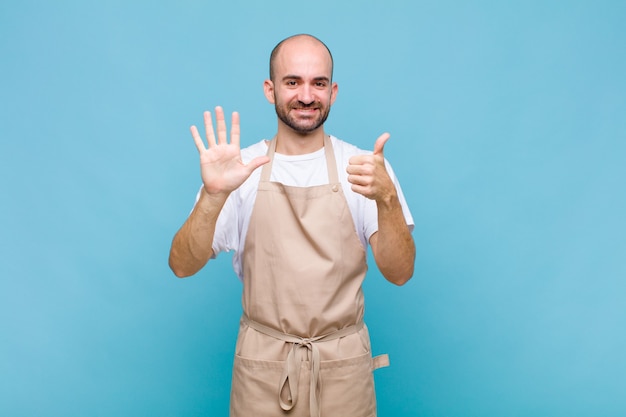 Uomo calvo che sorride e sembra amichevole, mostrando il numero sei o sesto con la mano in avanti, conto alla rovescia