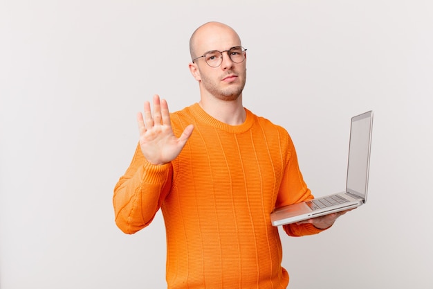 Uomo calvo con il computer che sembra serio, severo, dispiaciuto e arrabbiato che mostra il palmo aperto che fa un gesto di arresto