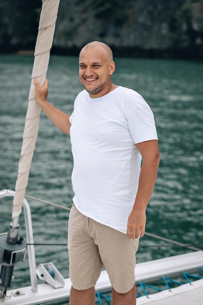 Uomo calvo in abiti bianchi che sorride alla telecamera sullo yacht. Phuket. Tailandia.