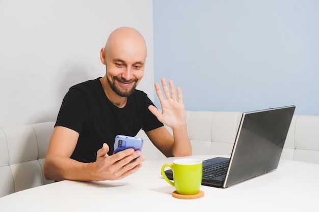 Uomo calvo sorridente con la barba in maglietta nera che lavora al taccuino a casa vista laterale